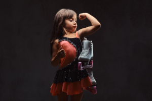 Joyful little girl dressed in skater dress holds ice skates.