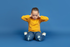 Portrait of sad little girl sitting on blue studio background, autism concept